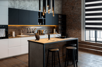 Nowoczesna kuchnia z centralną wyspą, dwoma stołkami i wiszącymi lampami. W pomieszczeniu znajdują się ciemne szafki, rustykalna ściana z cegieł i pasiaste żaluzje na dużym oknie, tworzące kontrast z ciepłym oświetleniem.